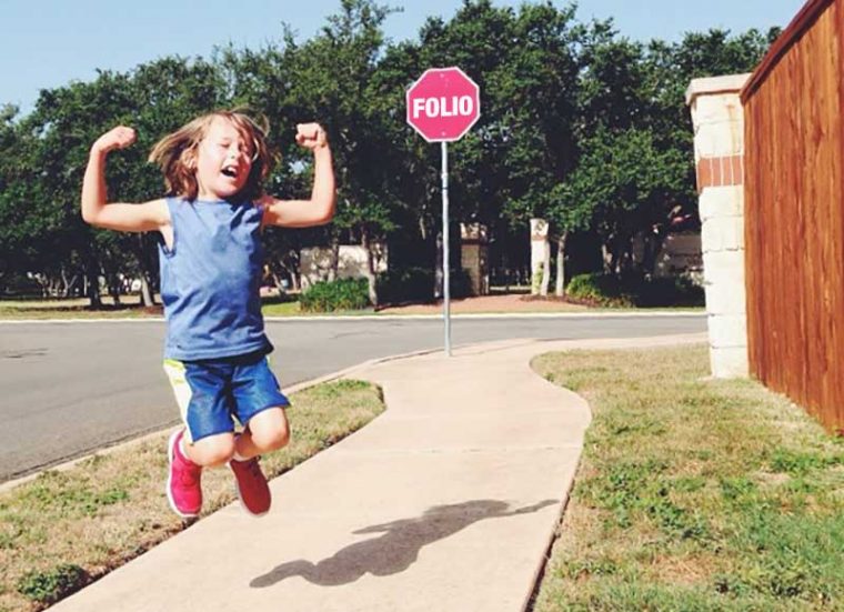 A girl jumps in the air in joy in front of a sign reading -- Folio