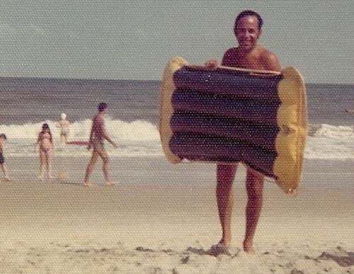 1970s vintage photo of man holding a surf mat at a beach