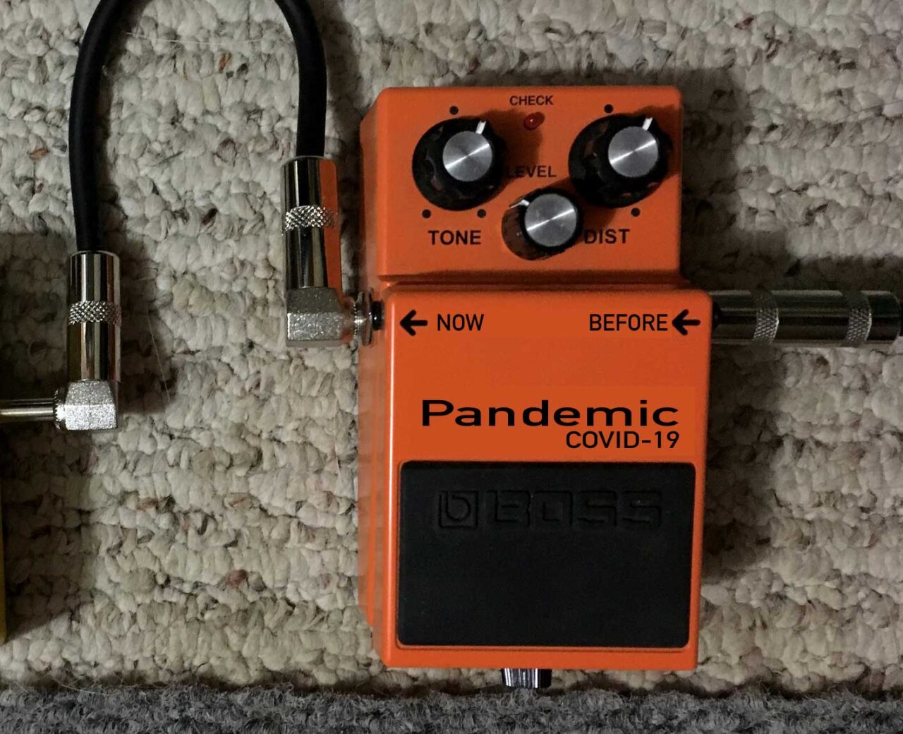 An orange guitar distortion  effects pedal with input and output cables, the brand name has been changed to read-- Pandemic COVID-19-- and the input/output labels changed to before/now