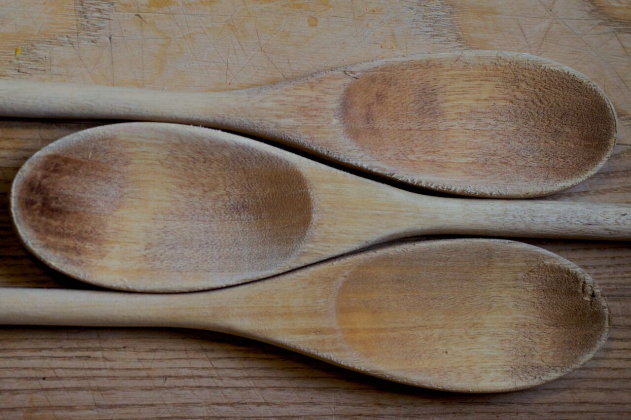 Three old wooden spoons nestled together to form a whole, all sitting on a wooden cutting board of similar texture.