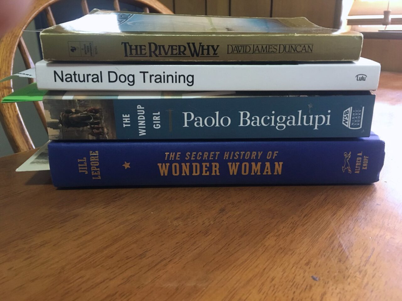 A stack of four unread books sitting on a wood table.