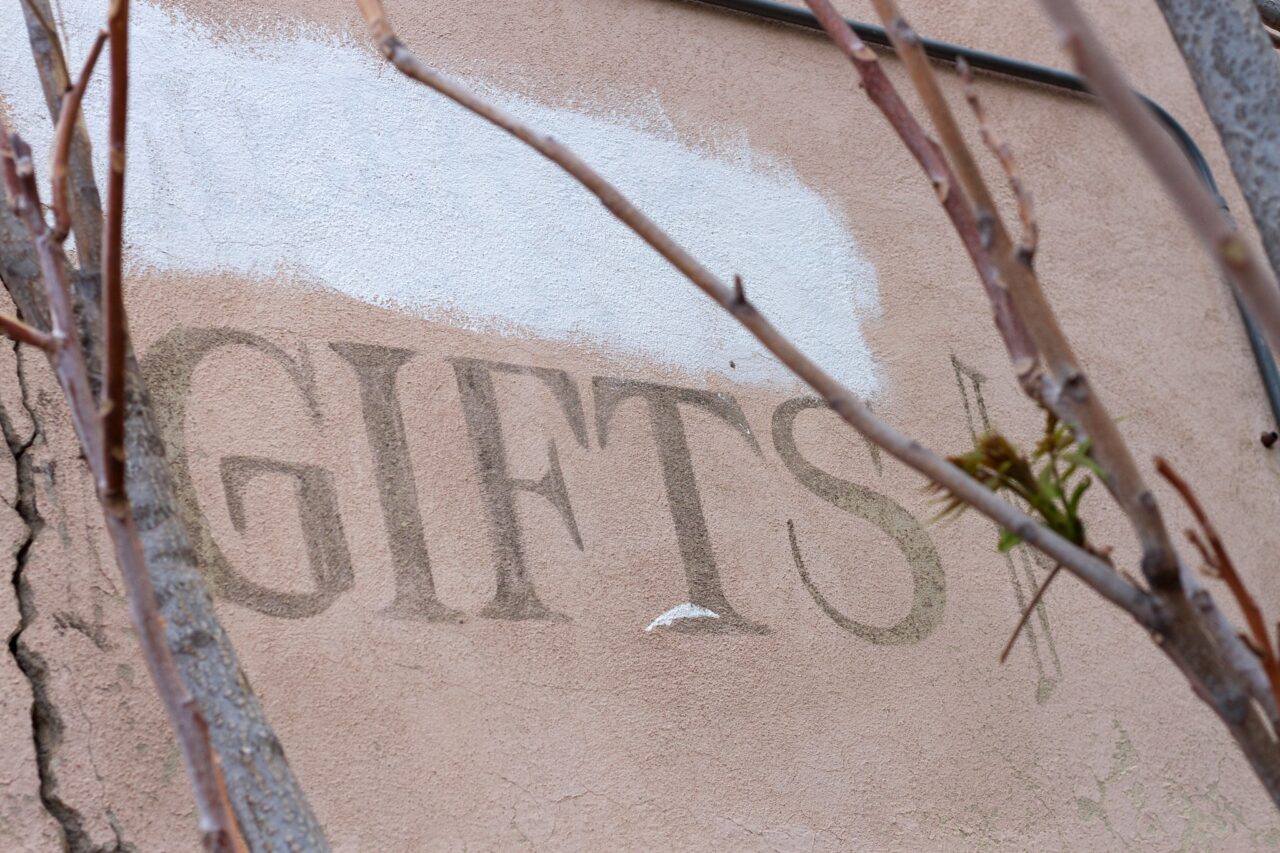 Painted on an old building wall in large text is the word Gifts