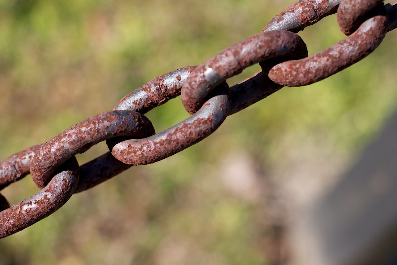 A section of a chain of large metal links, much covered in rust, extending from lower left to top right.
