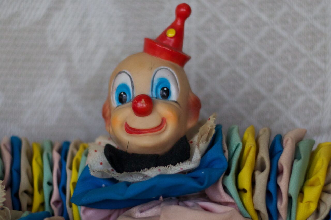A big eyed towy clown figure with a bulbous blue and yellow suit, stares out creepily.