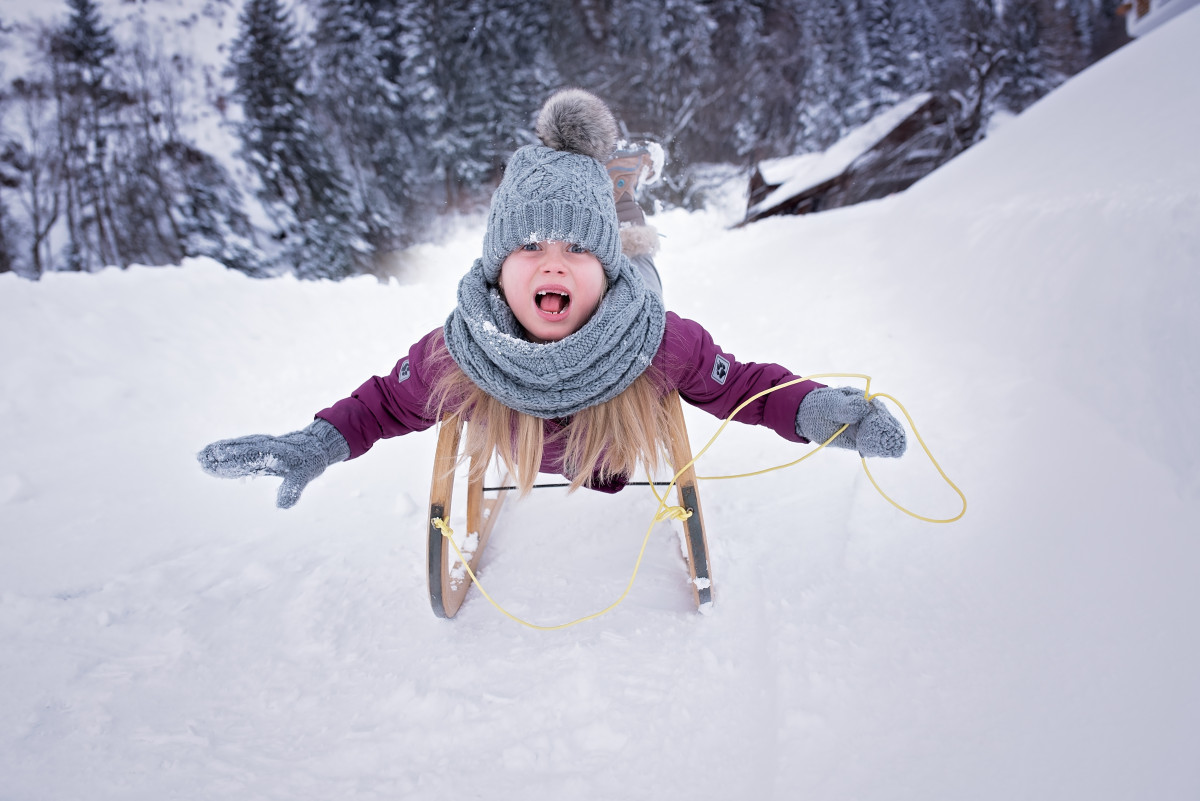 Young child with qrms out, big smile ridding a sled downhill in the snow.