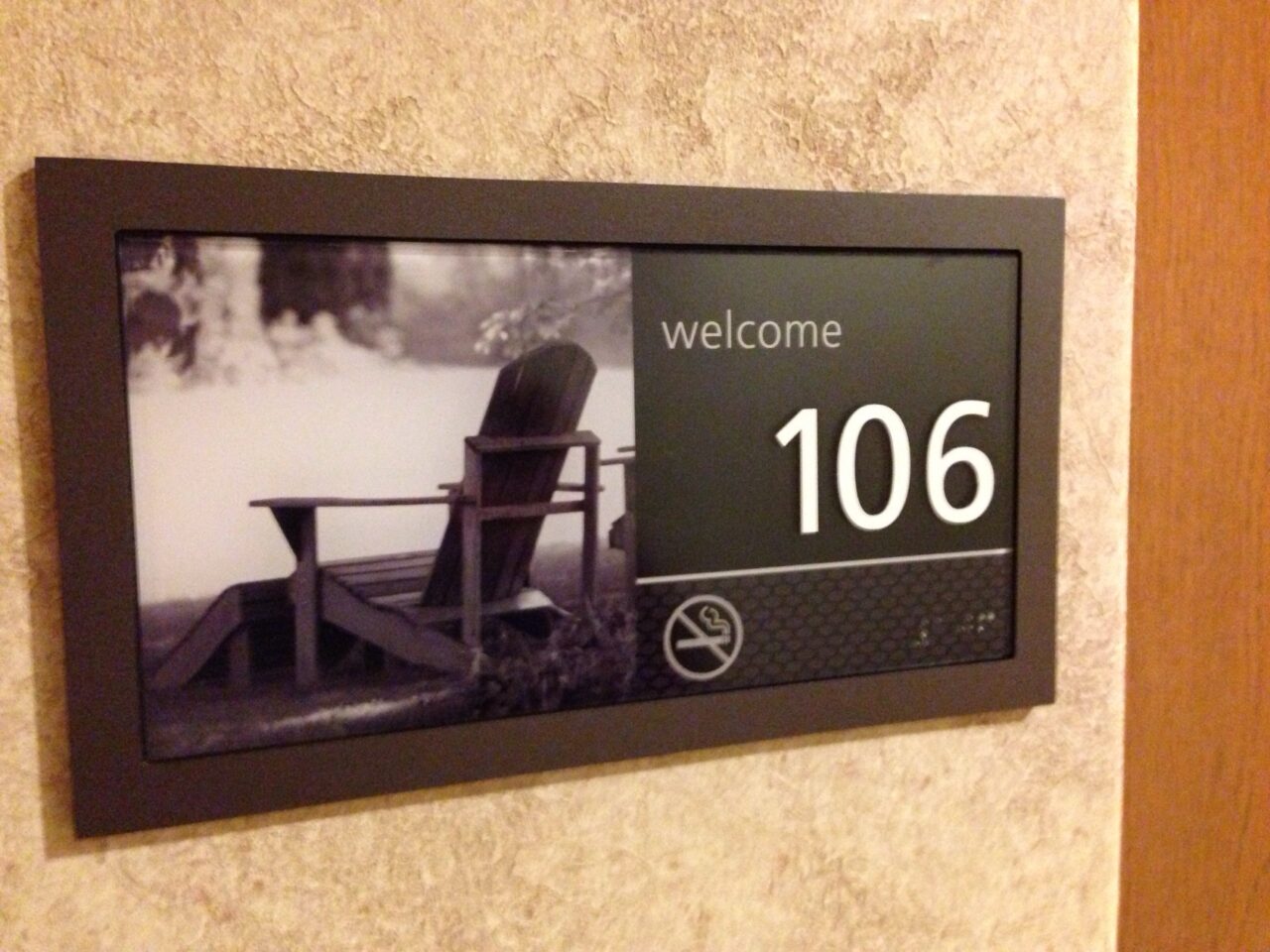 Hotel door sihn with a photo of an Adirondack chair, the word Welcome, and number 106.
