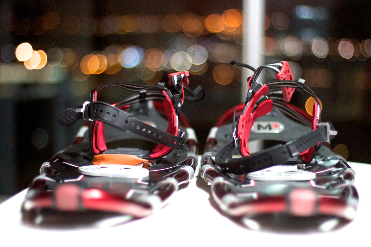 Rear view of red metal snowshoes sitting in front of a window with bright bokeh style lights out beyond.