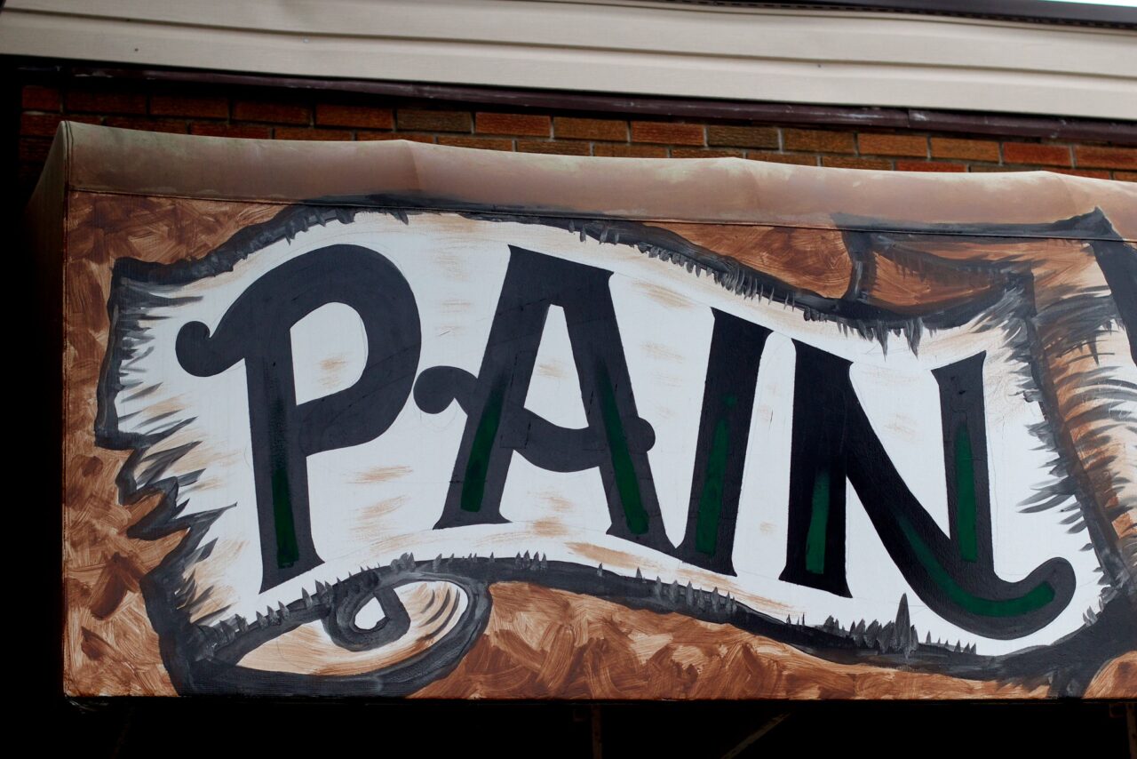 Painted sign, curved text on a white scroll reading Pain.