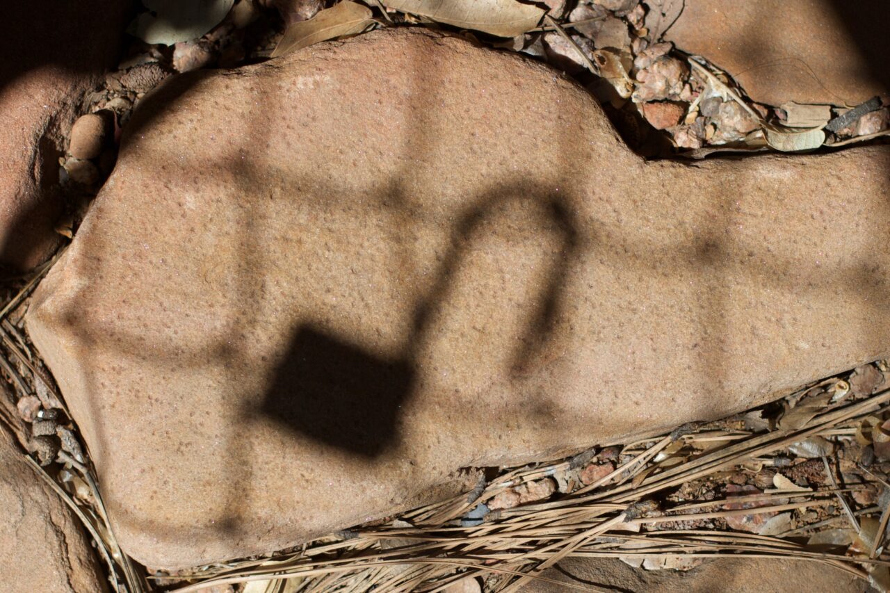 Shadow of an open padlock hanging on a fence cast on a slap og sandstone.