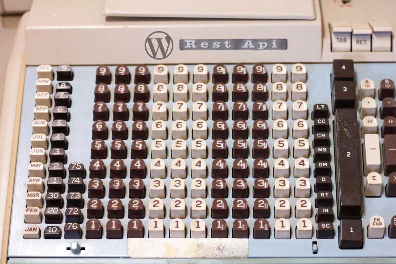 Old mechanical adding machine with numerous rose of buttons with numbers. The logo at the top which originally read Burroughs has been edited toi add a W logo, the WordPress icon, and embossed text reading Rest Api.