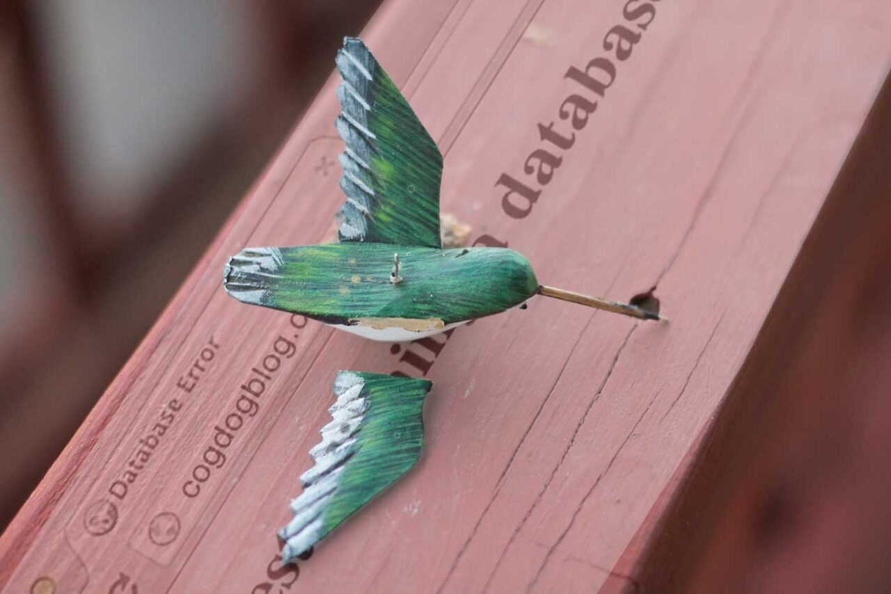 Small carved wood bird with a wing broken off sits on a fence railing. Superimposed on top is the database connection error that has been showing up this week on my wordpress blog.