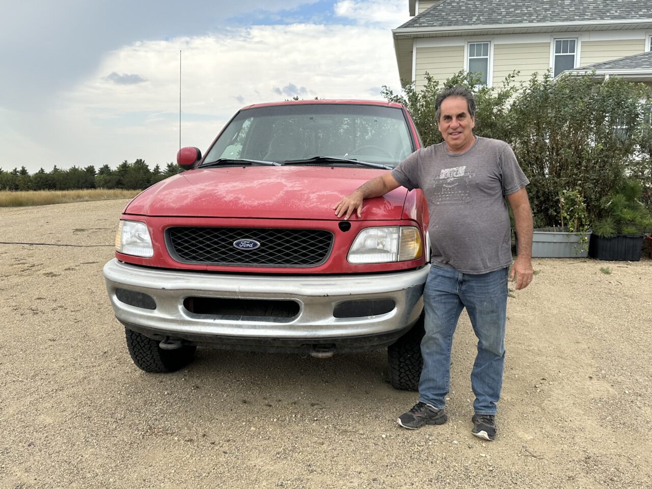 Man standing in front of red pickup truck, pointing to hole in front