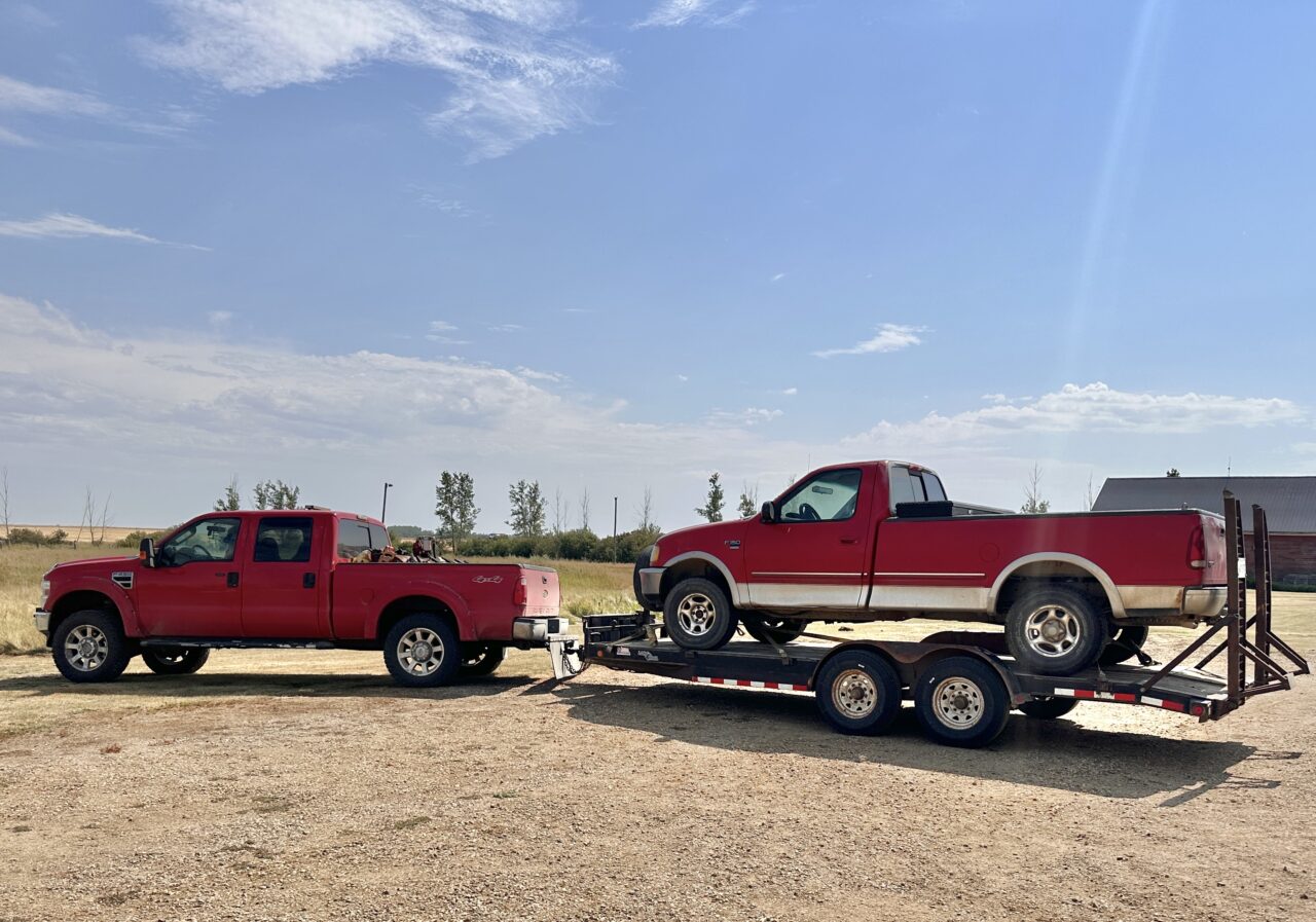 Red truck loaded on trailer being pulled by bigger red truck.