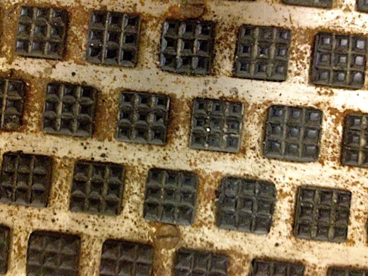 A grid of repeated metallic, weathered shapes, each of them the same square shape with a 3 by 3 matrix of smaller squares within, each with nine internal objects.